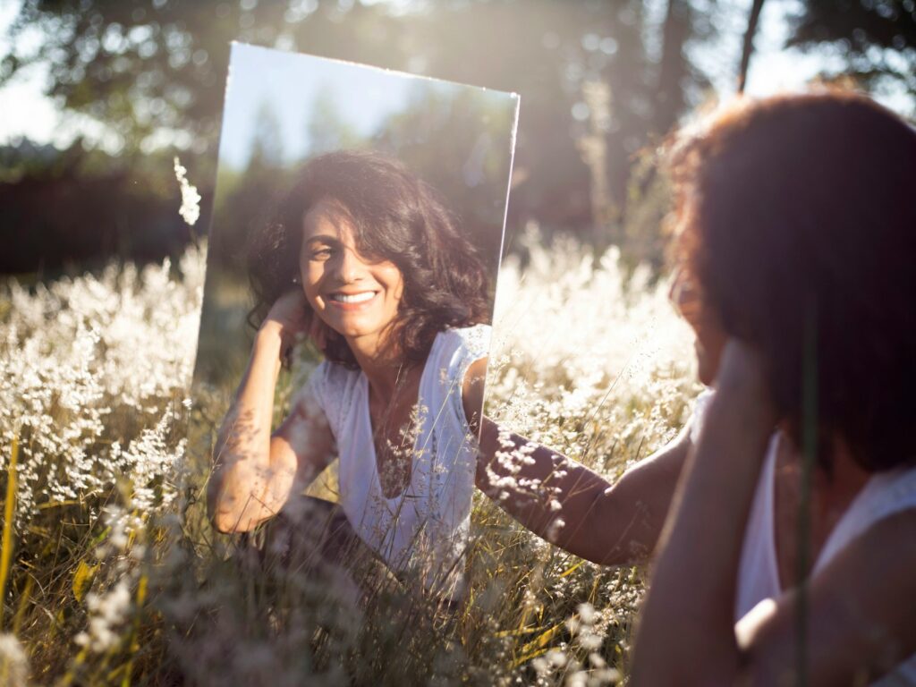 A woman in blue and white floral shirt holding a mirror. It shows her reflection.