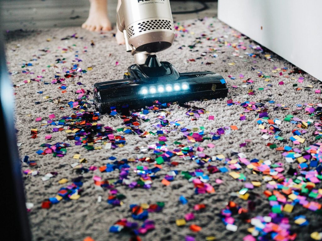 A person learning how to adult by using a vacuum to clean a carpet that has confetti on it.