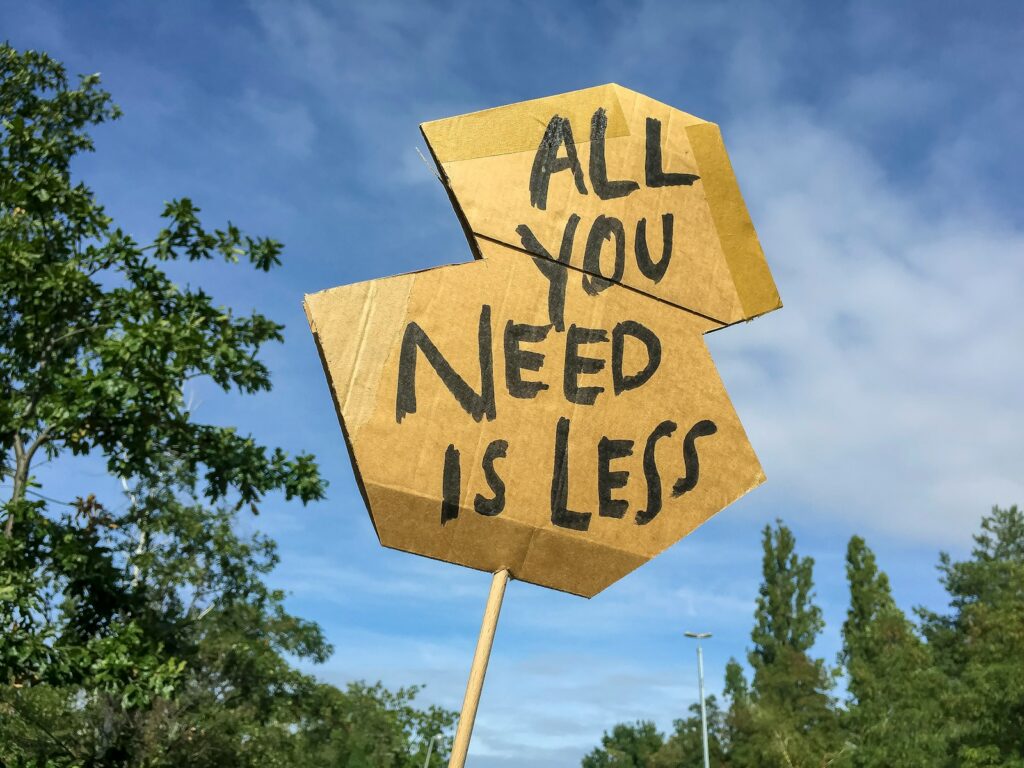 A cardboard sign that says "all you need is less." This is going to echo how to free up what is important to you as a responsibly broke person.