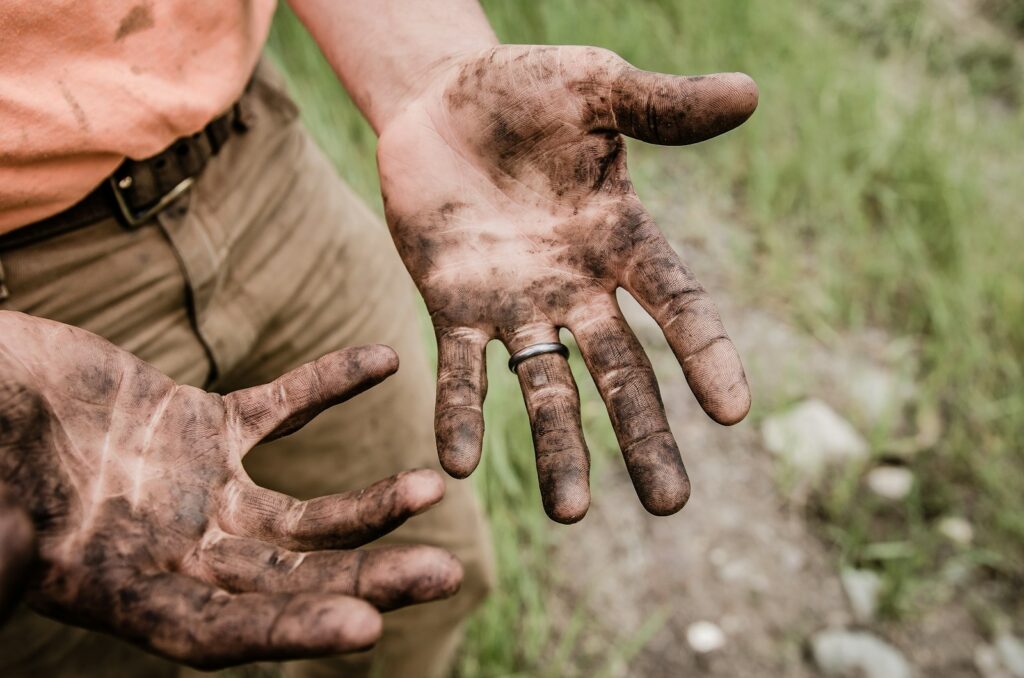 A responsibly broke man with his hands covered with mud. He's working hard today so he can have easier days ahead.