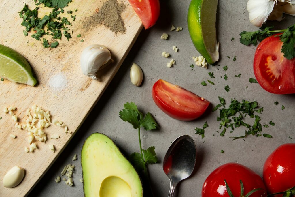 Sliced tomatoes and avocados on the chopping board and grey table with seasonings surrounding it. All of this is leads into the next part of learning how to be an adult.