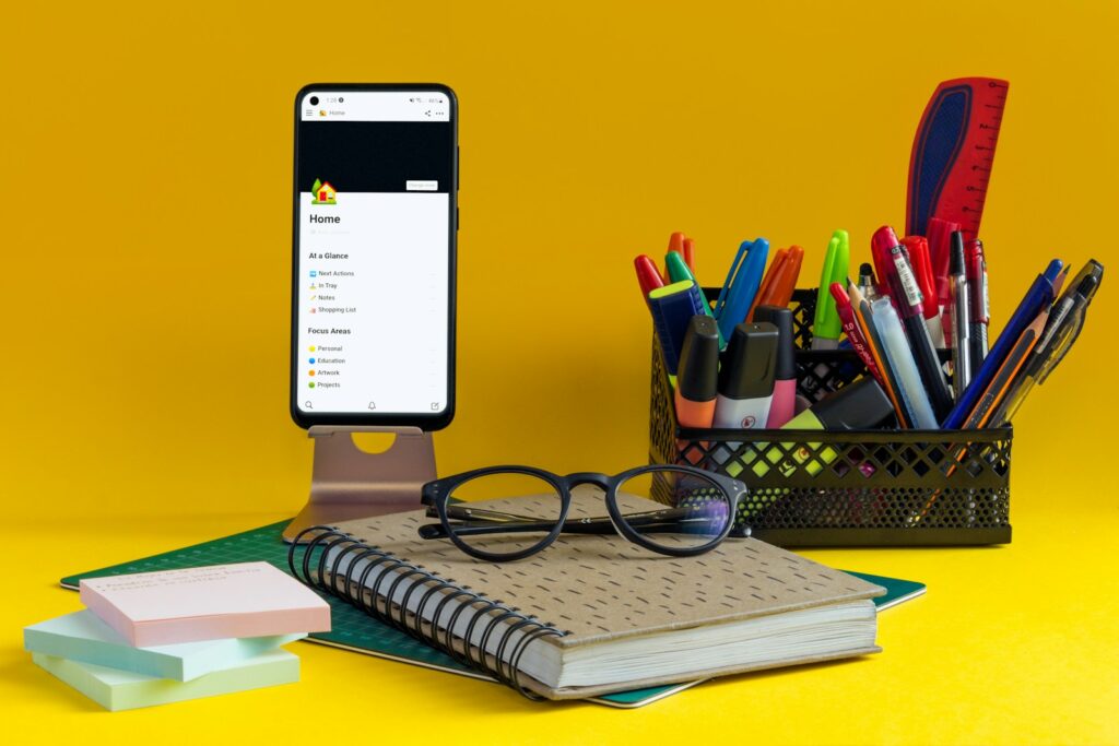 A notebook, pen, glasses and cell phone on a yellow background. In this part, you're going to organize your schedule based off of your priorities so you can make time to do the things you need and want to do.