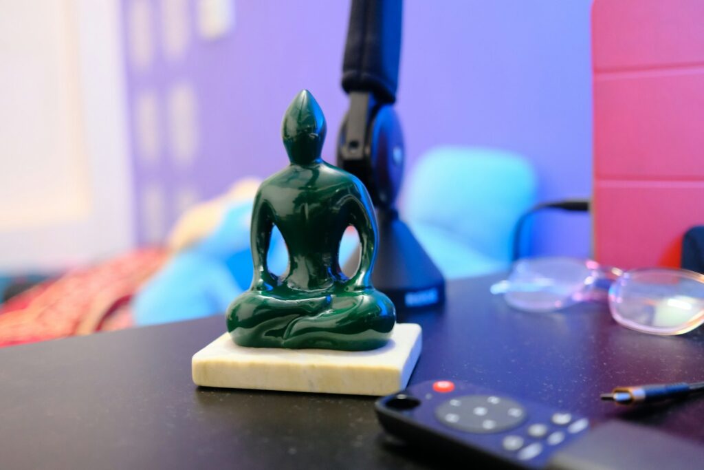 A small statue of a person sitting on a table next to a remote control. This symbolizes how important it is to make time in slowing down and grounding yourself.